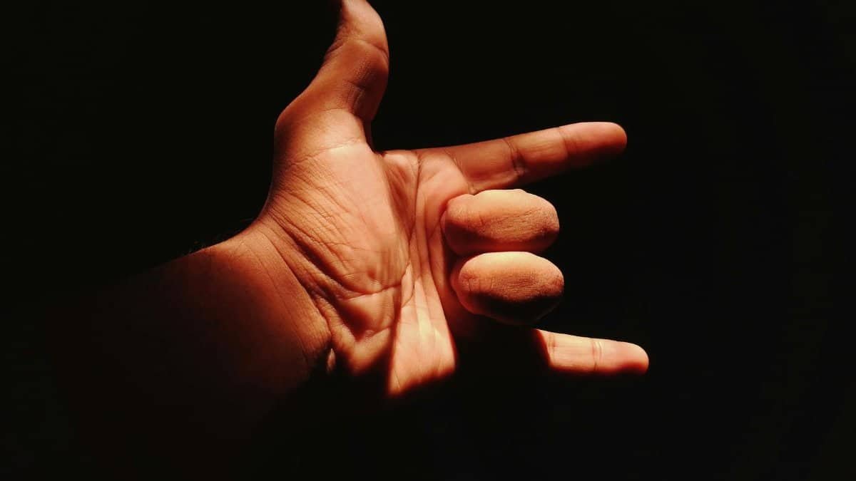 A close-up of a hand making the shaka sign, dramatically lit against a dark background.