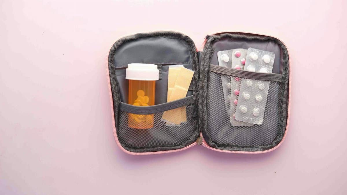 Open first aid kit with pill bottle, blister packs, and band-aids on a pastel background.