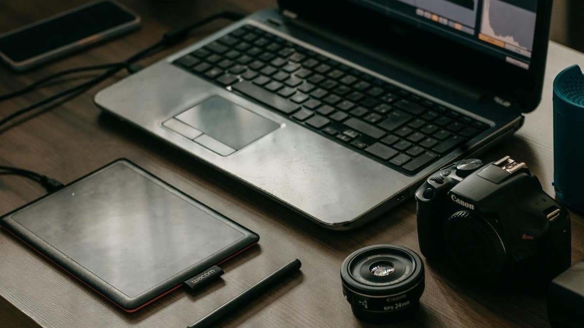 Laptop, camera, lens, and graphic tablet on a desk for digital creatives.