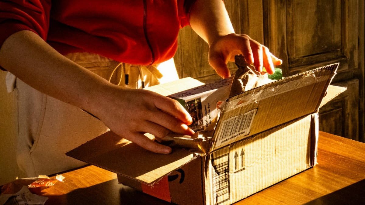 A person unboxing a package, revealing curiosity and anticipation in a warmly lit setting.