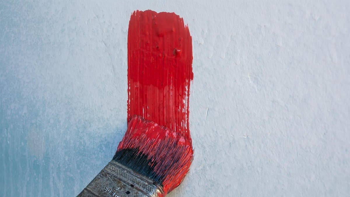 A paintbrush applies vibrant red paint to a white wall, showcasing DIY home improvement.