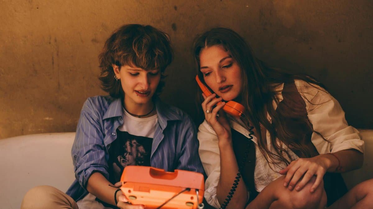 Two young adults using a vintage orange phone, sitting in a cozy indoor setting.