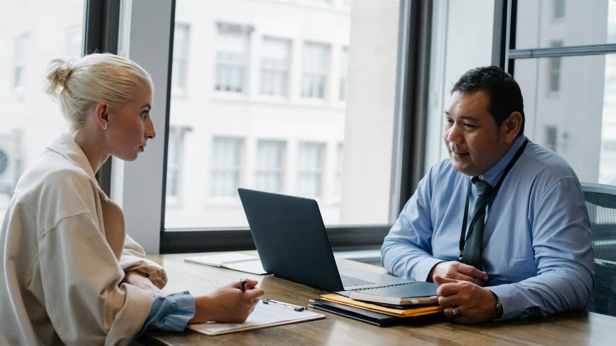 Ethnic boss asking question to female candidate filling information form on clipboard during hiring meeting
