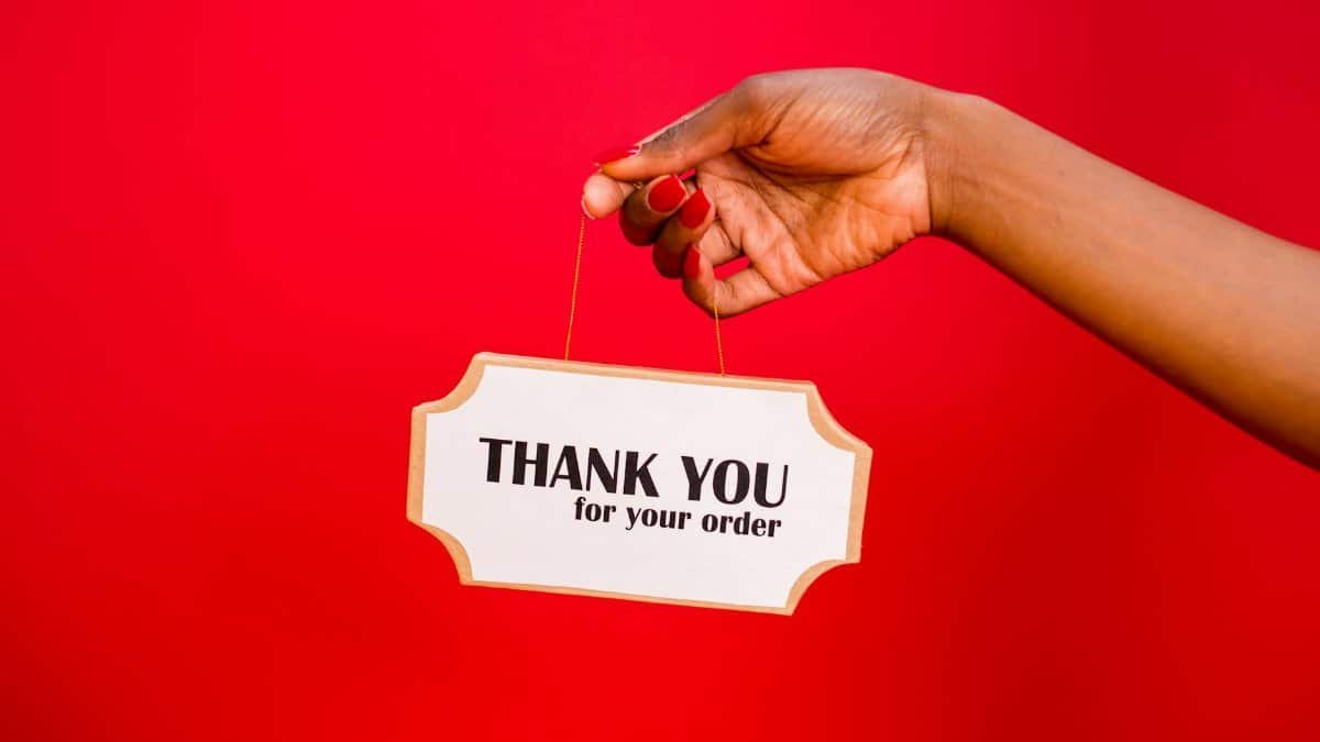 A person holding a thank you sign against a vibrant red background.