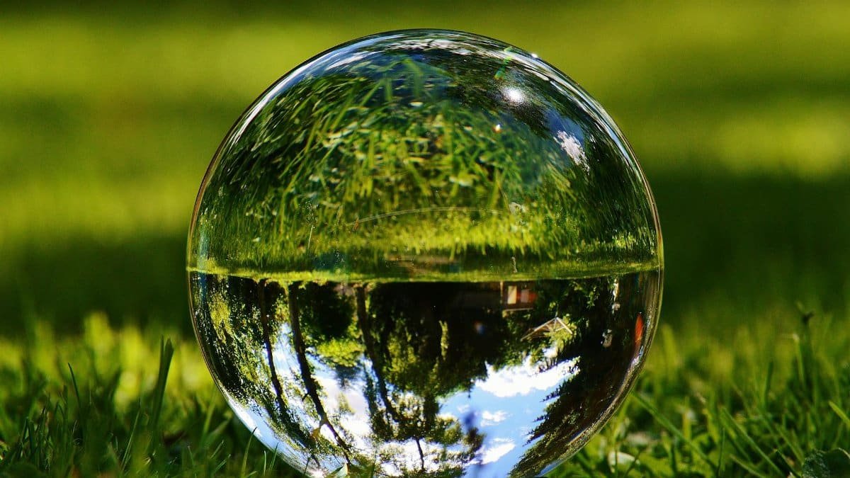 Close-up of a glass crystal ball on grass reflecting an upside down outdoor scene.