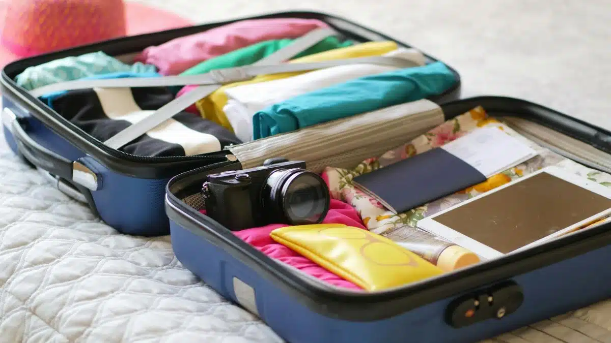 Open suitcase with camera, clothes, and passport, ready for a summer vacation.