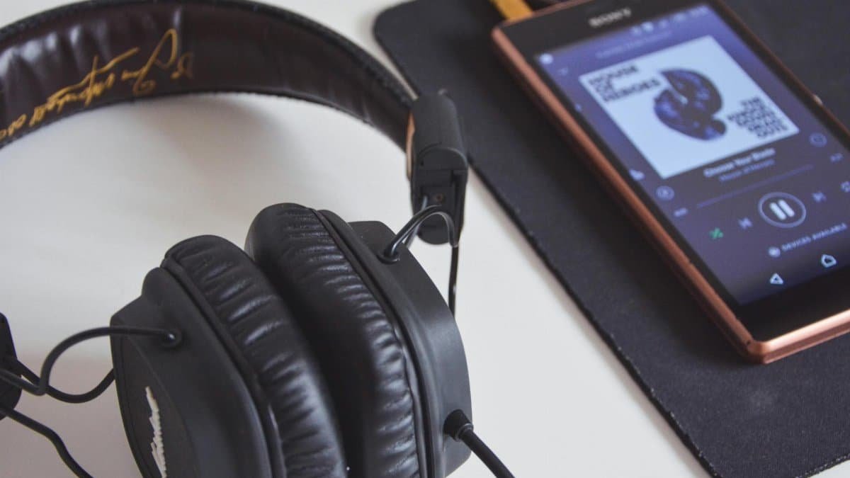 A close-up of headphones and a smartphone playing music on a desk.