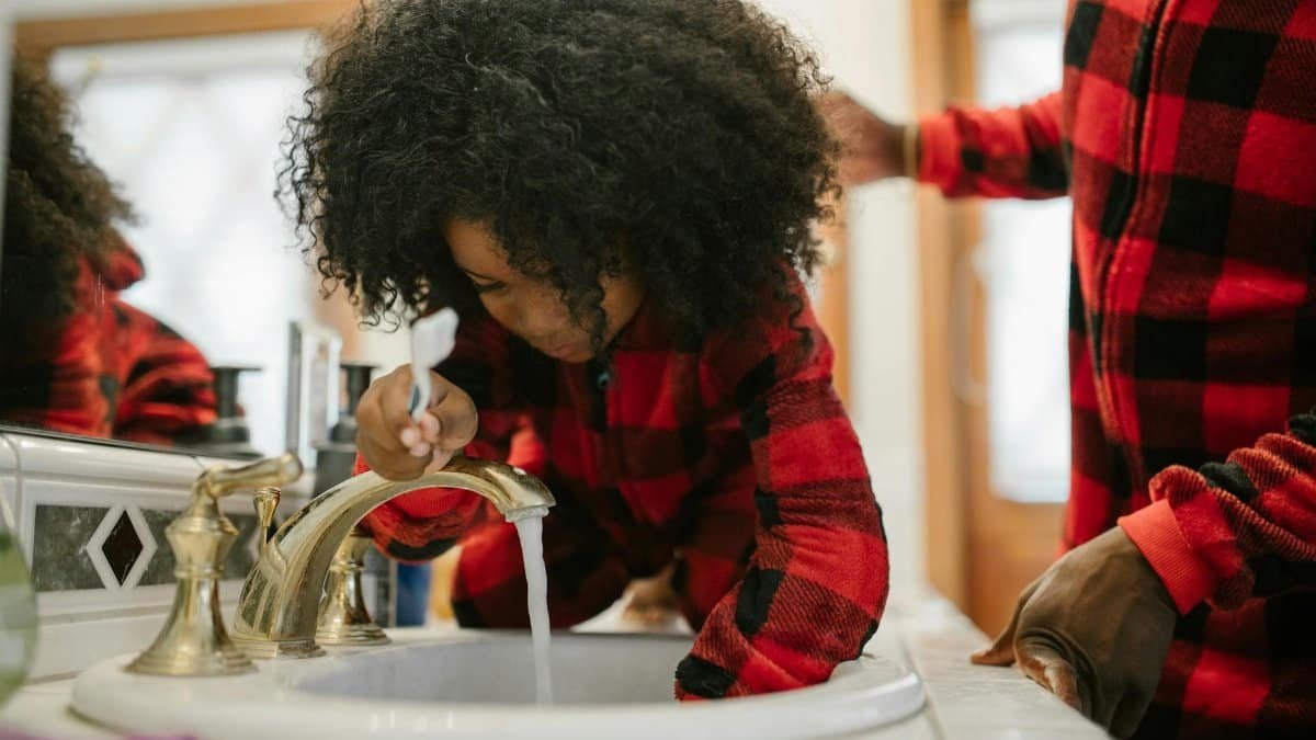 A father helps his daughter brush her teeth at the bathroom sink, highlighting family routines.