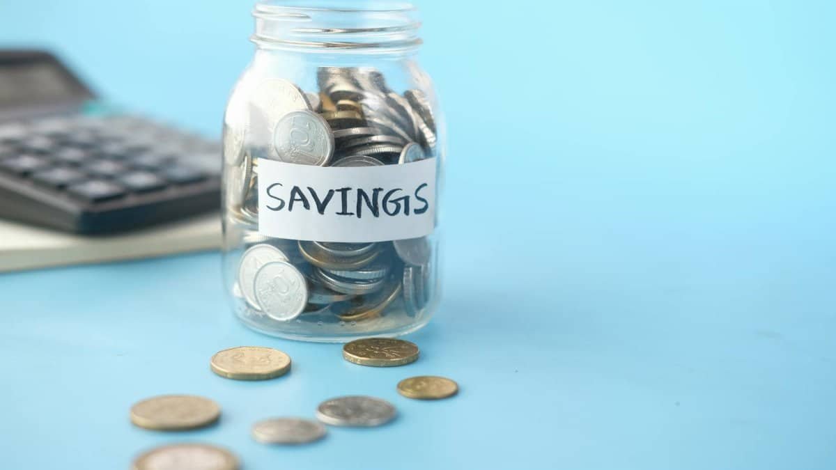 Glass jar labeled 'Savings' filled with coins, beside a calculator on a blue background.