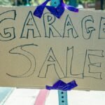 A handwritten garage sale sign taped on cardboard, displayed outdoors.