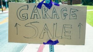 A handwritten garage sale sign taped on cardboard, displayed outdoors.