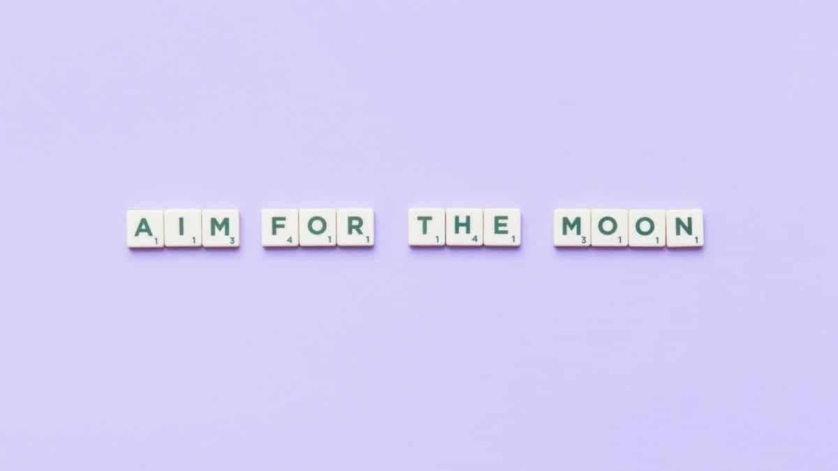 Scrabble tiles forming 'Aim for the Moon' on a purple background inspire motivation.
