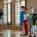 A coach instructing a diverse group of children during a gym class in a school sports hall.