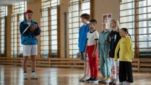 A coach instructing a diverse group of children during a gym class in a school sports hall.