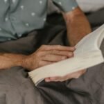 Close-up of an adult reading a book in bed, wrapped in a cozy blanket, enjoying leisure time indoors.