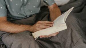 Close-up of an adult reading a book in bed, wrapped in a cozy blanket, enjoying leisure time indoors.