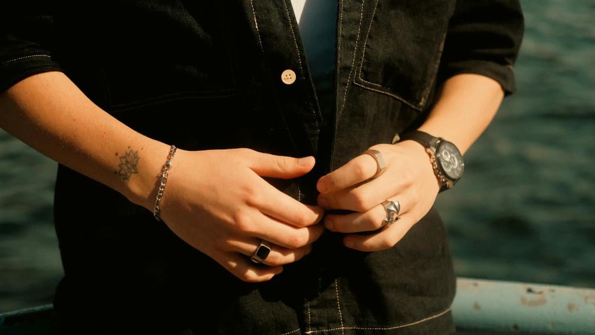 Detail shot of hands wearing rings, bracelet, and watch by the water.