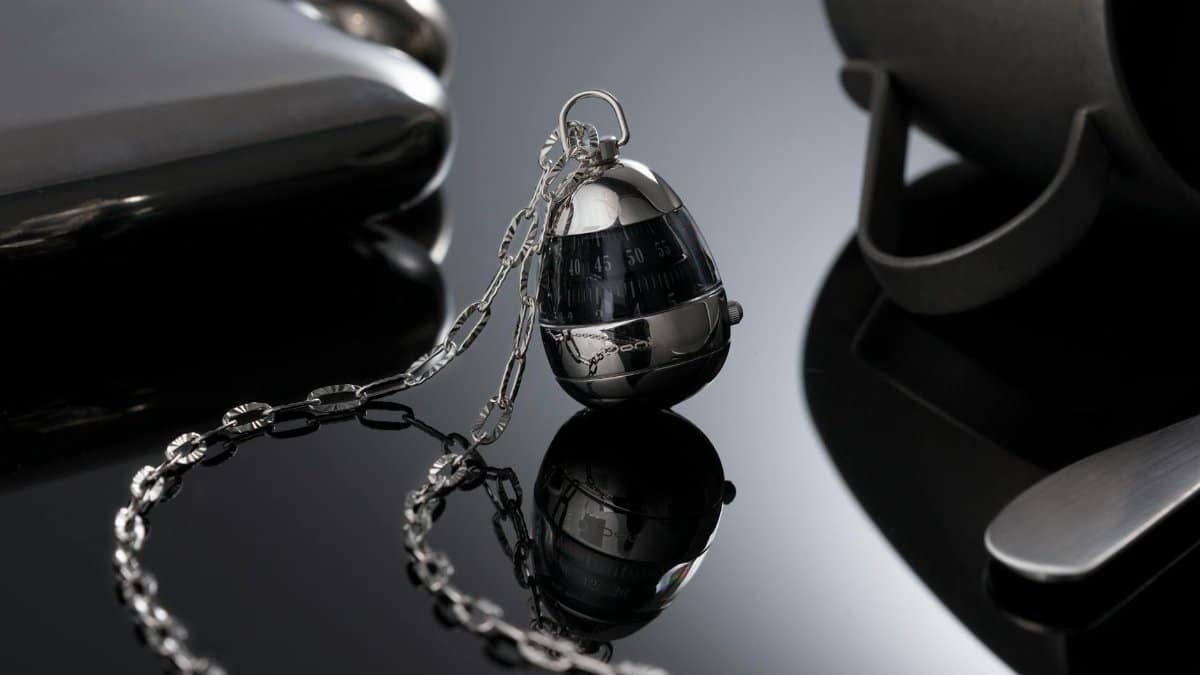Sophisticated silver egg timer with chain reflecting on a sleek black surface, symbolizing luxury.