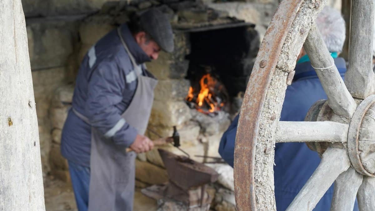 Blacksmith forging metal beside fire in rustic workshop, creating artisanal crafts.