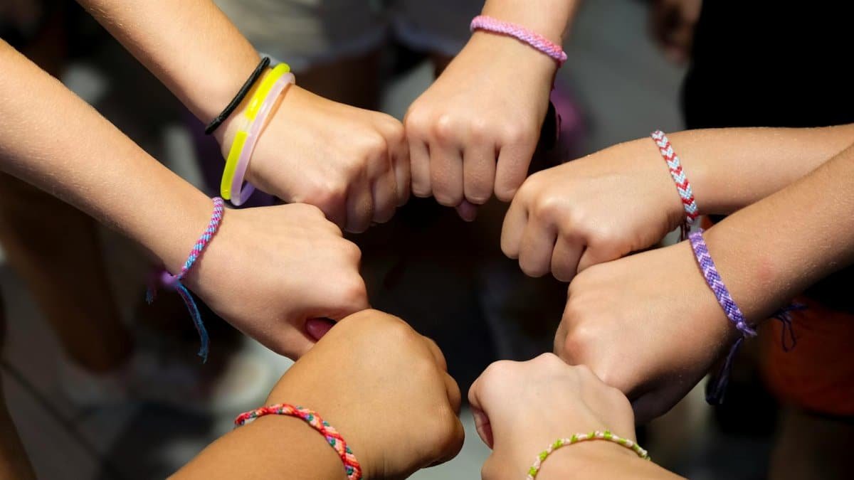 A diverse group of hands wearing colorful friendship bracelets in unity.