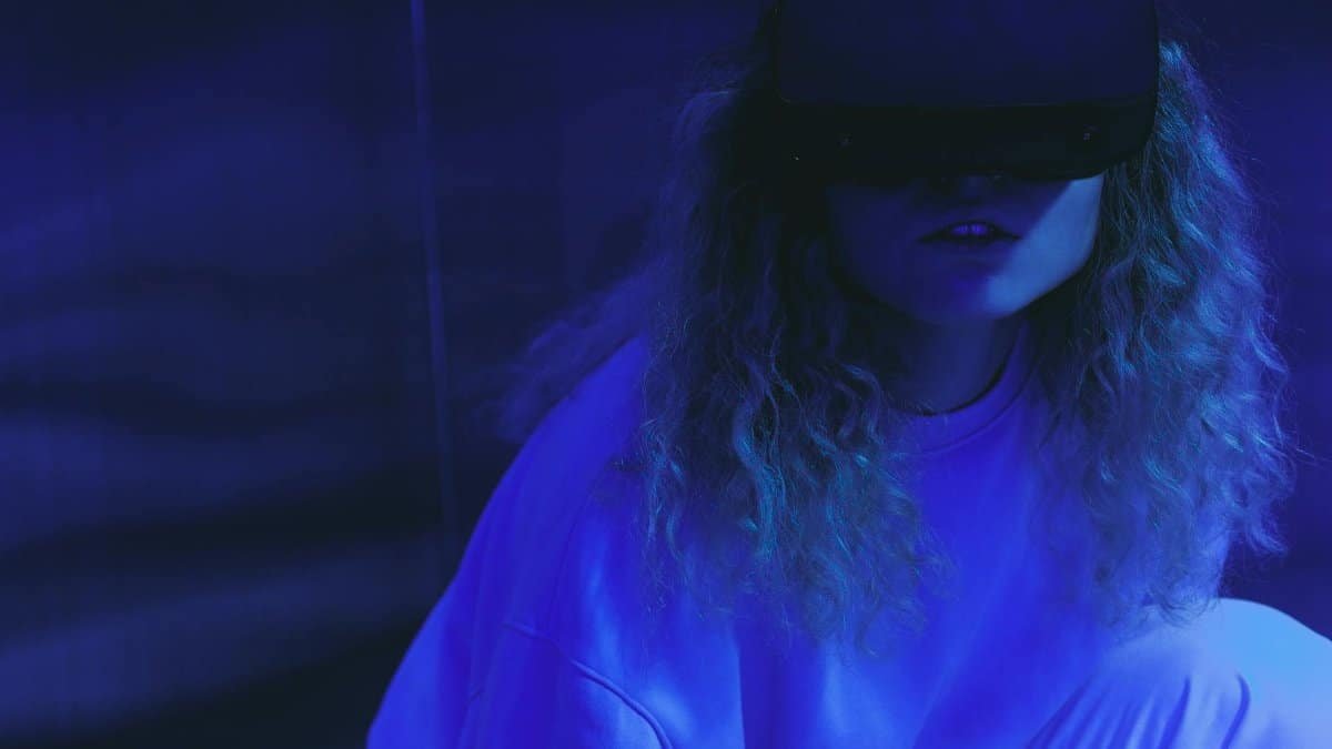 A woman wearing a VR headset enjoys a virtual reality experience in neon lighting.
