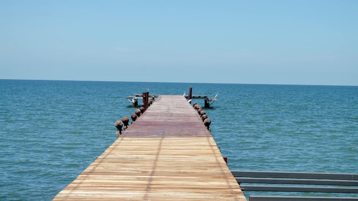 A tranquil scene of a wooden pier extending into a calm blue sea under a clear sky, perfect for escape and relaxation.