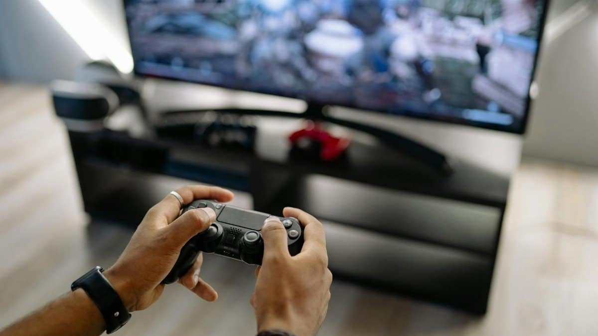 Close-up of hands holding a gaming controller while playing video games indoors.