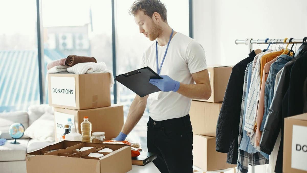 A volunteer organizes charitable donations and clothing indoors with a clipboard.