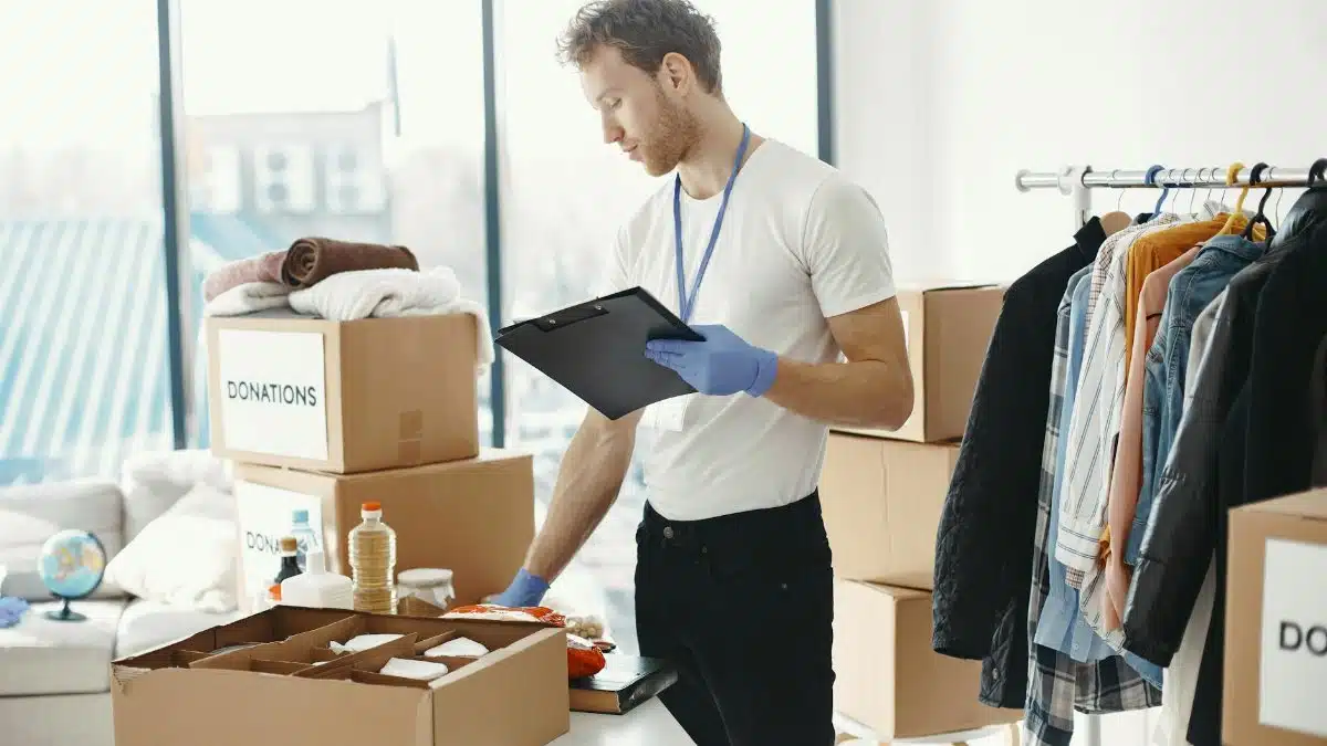 A volunteer organizes charitable donations and clothing indoors with a clipboard.
