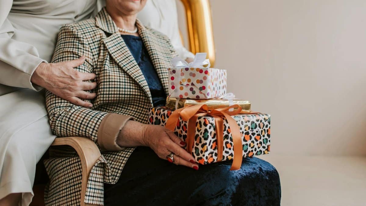 Senior woman receives gifts during indoor celebration with family support.