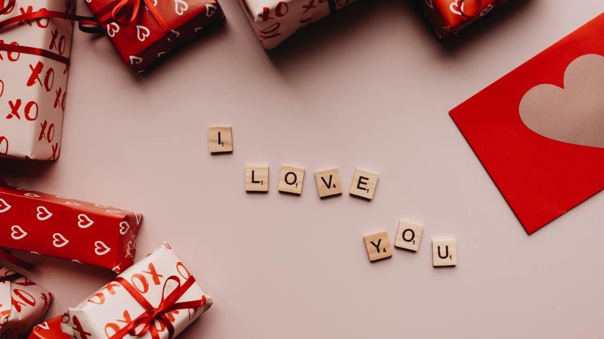 Valentine's Day gifts with heart-patterned wrapping paper and 'I Love You' spelled with Scrabble tiles.