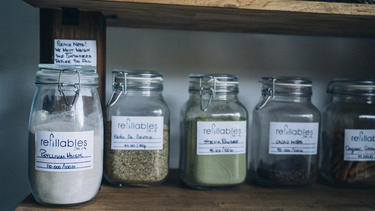 Assorted refillable glass jars with organic goods on a wooden shelf.