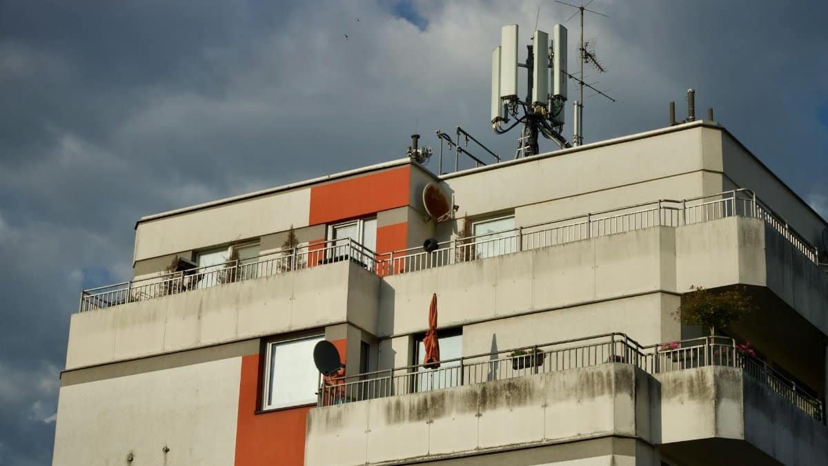 Photo of a modern apartment building with a rooftop antenna under a cloudy sky.