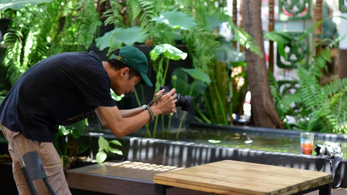 Side view of a photographer taking pictures of a natural scene in a garden setting.