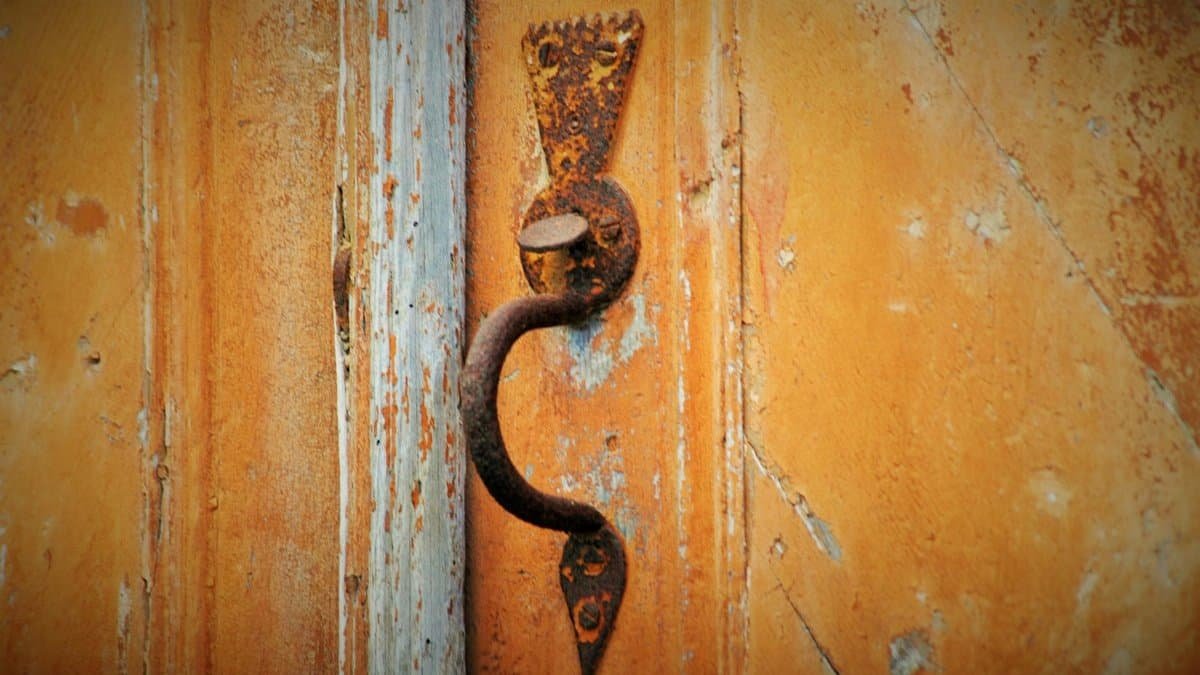 Close-up of a vintage rusty door handle on a weathered wooden door, showcasing rustic charm.