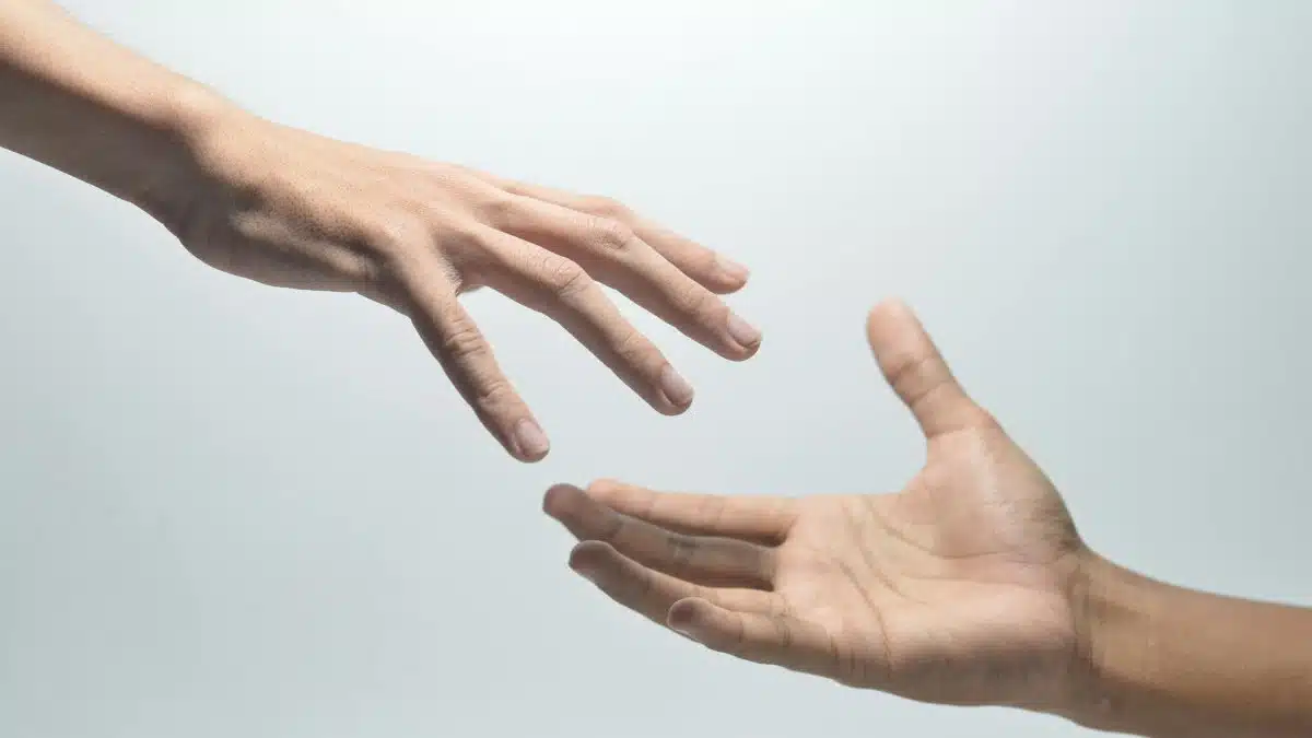 Close-up of two hands reaching towards each other on a neutral background, symbolizing connection.