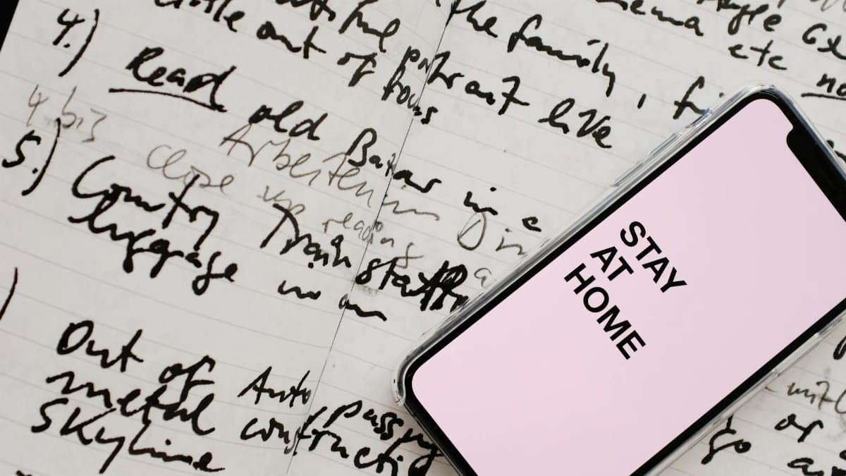 Abstract image of a smartphone displaying 'Stay At Home' over handwritten notes promoting safety and organization.