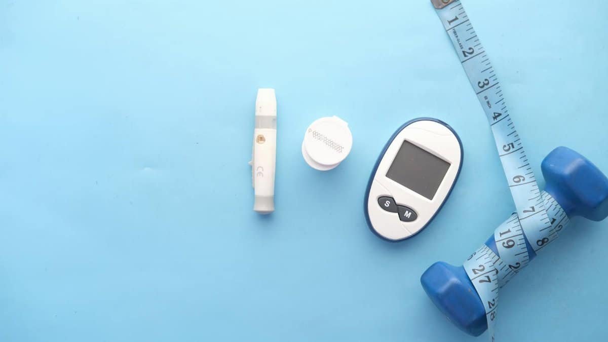 Top view of fitness and health equipment including dumbbell, glucometer, and measuring tape on a blue background.