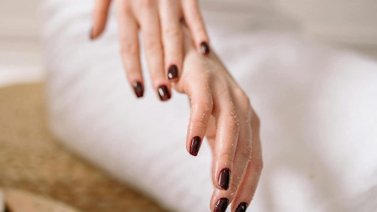Close-up of a woman's hand with dark polished nails against a spa backdrop.