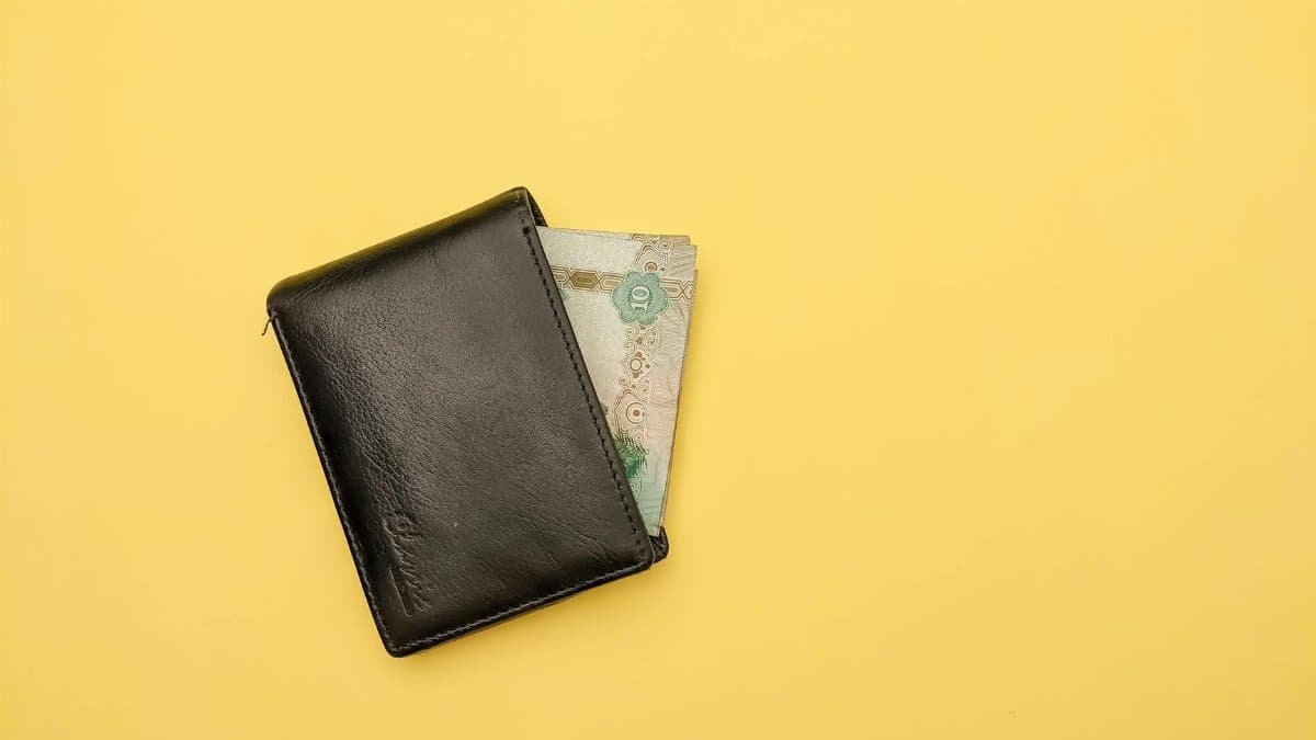 A black leather wallet partially open with visible paper currency on a bright yellow background.