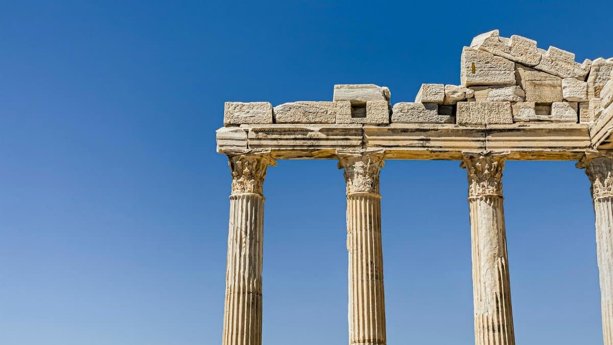 Columns of an ancient Greek temple stand tall against a bright blue sky.