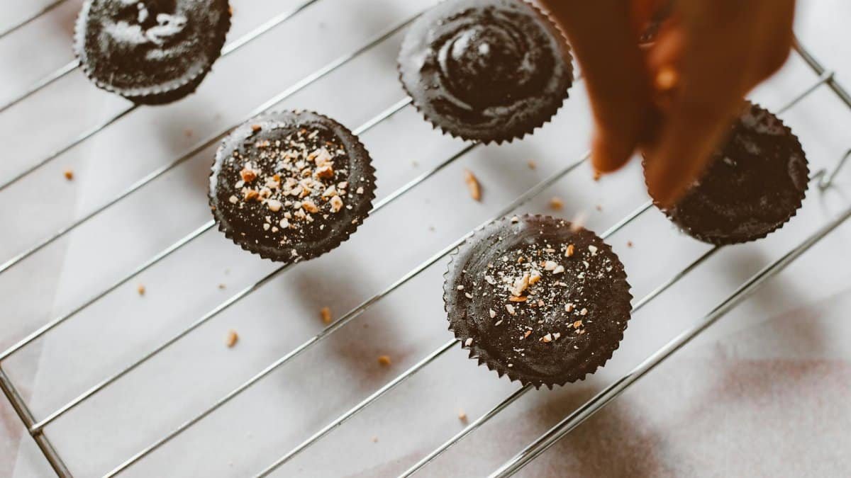 Freshly baked chocolate muffins sprinkled with nuts on a cooling rack, a hand arranging them.