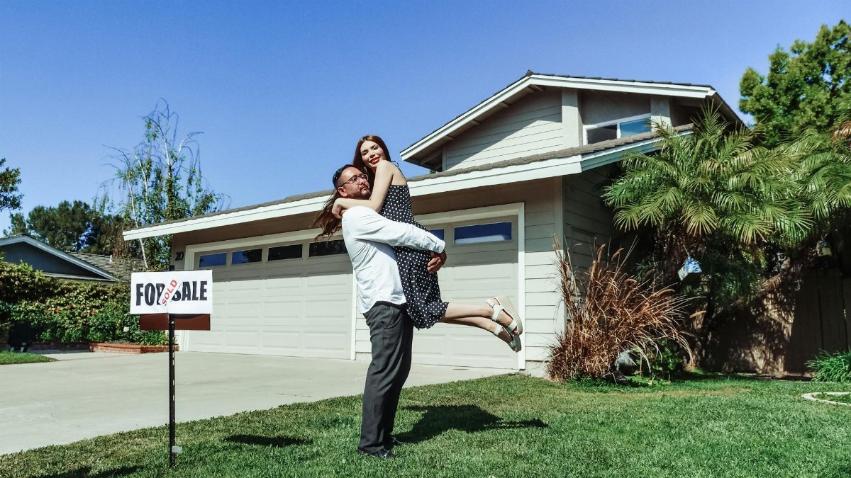 A joyful couple celebrating their new home purchase in front of a house with a sold sign.