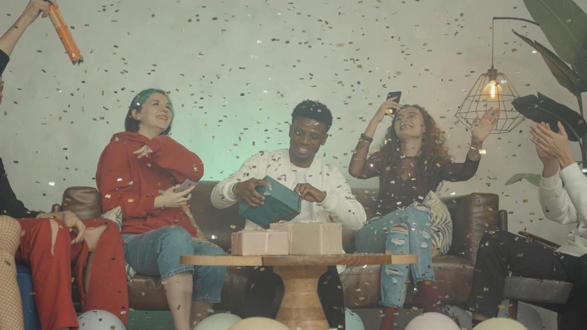 Group of friends celebrating indoors with gifts and confetti, creating a joyful atmosphere.