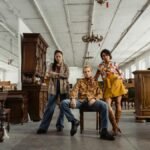 Stylish young adults posing amidst vintage furniture in a spacious warehouse setting.