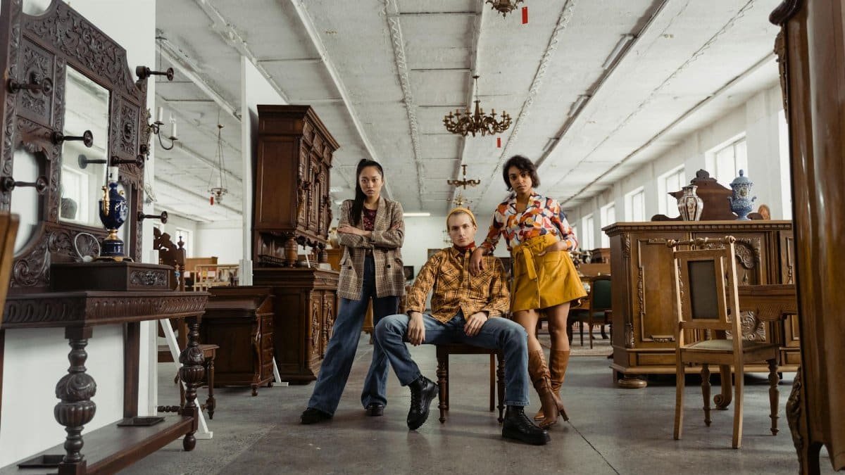 Stylish young adults posing amidst vintage furniture in a spacious warehouse setting.
