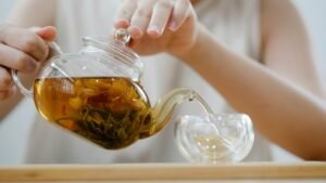 Adult woman pouring herbal tea into a cup, showcasing a cozy indoor tea ritual.