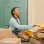 Young girl with braided hair sorting delivery packages on a porch.