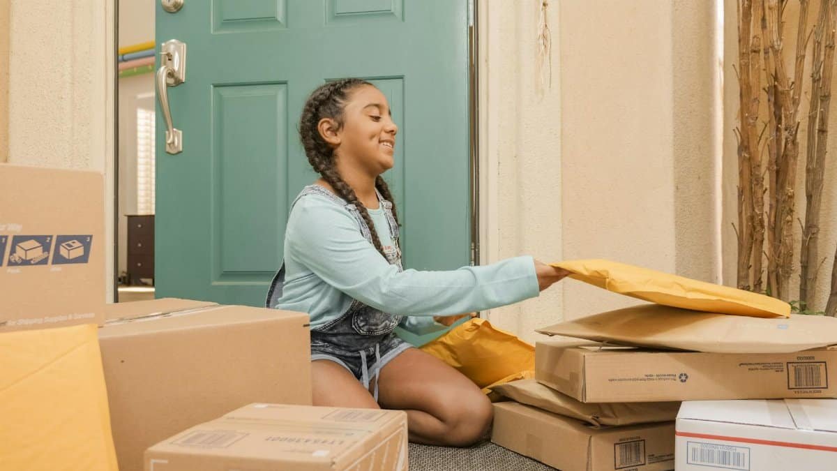 Young girl with braided hair sorting delivery packages on a porch.