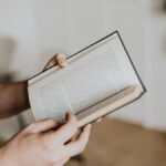 Close-up of a person holding and reading an open book indoors with a focus on hands and text.